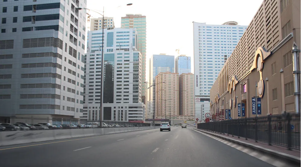 A bustling street view of Al Nahda 1 in Dubai, lined with shops, modern buildings, and busy traffic.