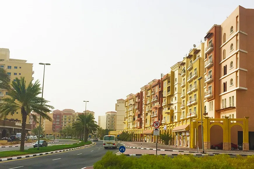 An outside road view of studio apartments for rent in Dubai International City, with modern buildings and a clear sky.